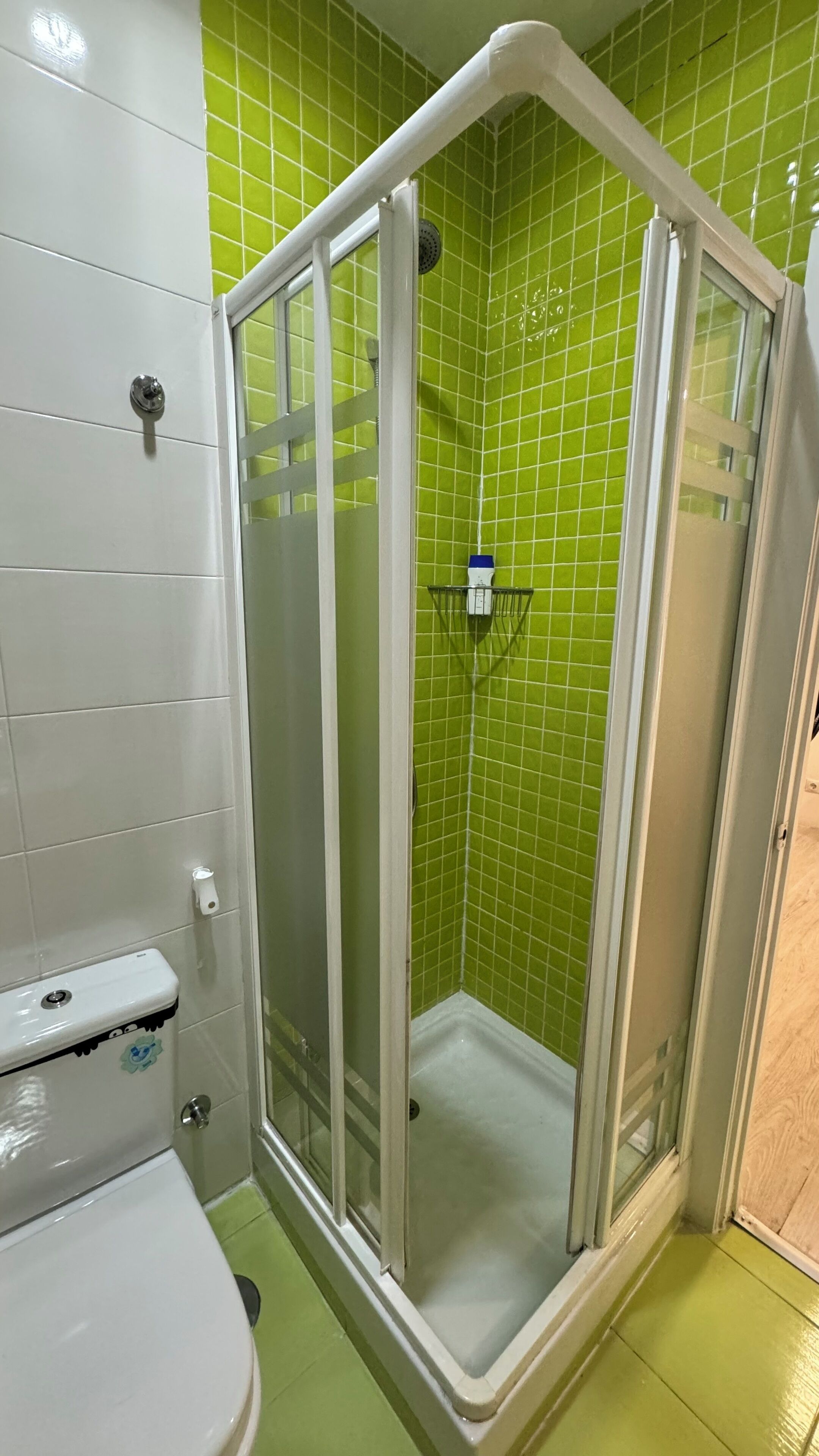 Un baño con inodoro blanco, cabina de ducha con azulejos verdes y lavamanos blanco.
