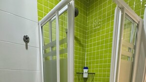 Une salle de bain avec des toilettes blanches, une douche carrelée de carreaux verts et un lavabo blanc.