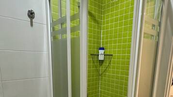 Un baño con inodoro blanco, cabina de ducha con azulejos verdes y lavamanos blanco.