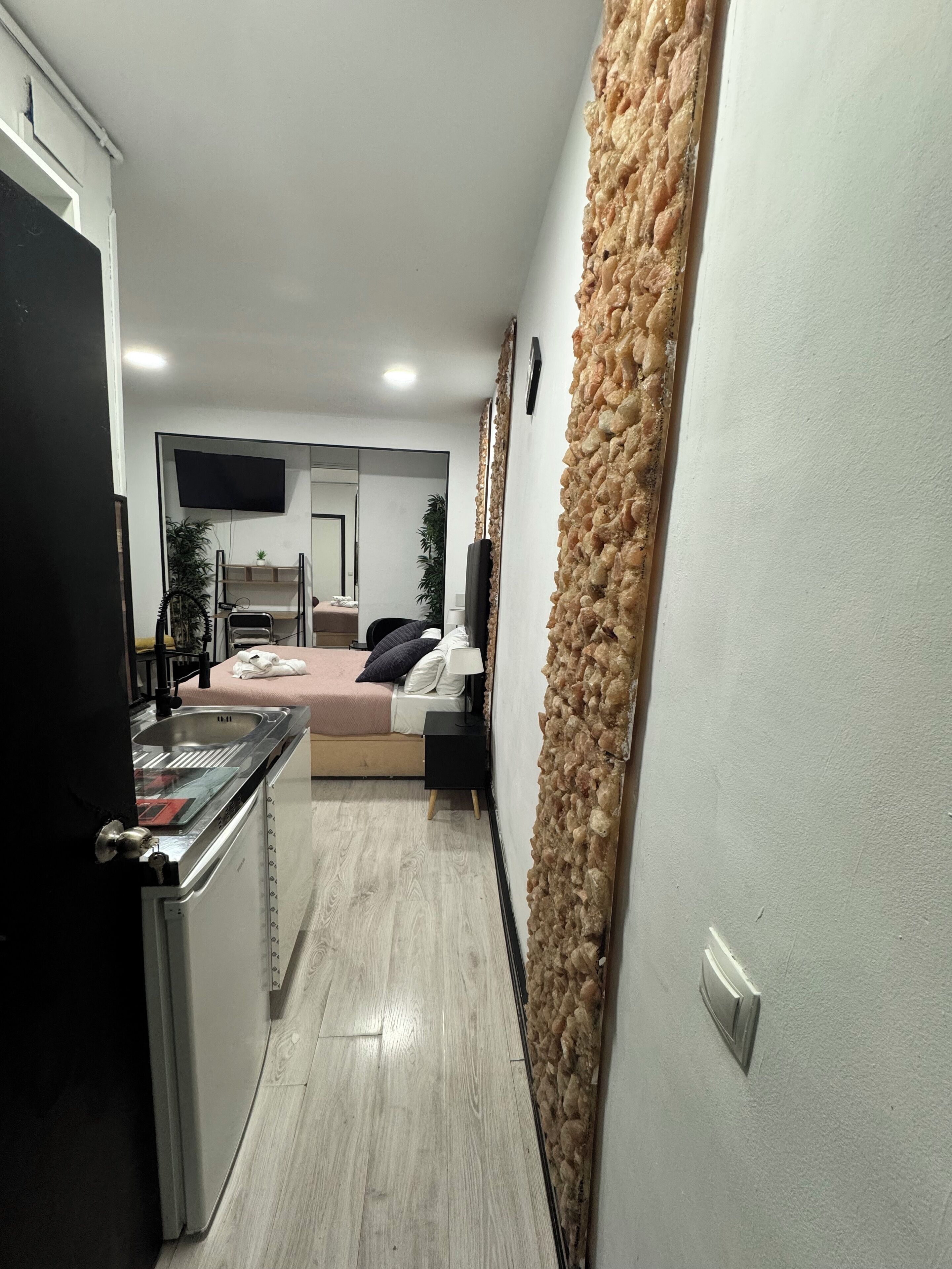 Una cocina moderna con estufa integrada, un pequeño comedor y un dormitorio con cama y televisor.