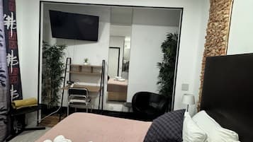 Una habitación de hotel con cama, escritorio, silla, televisor y espejo.