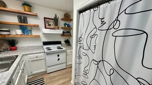 A modern kitchen with white cabinetry, a stove, and a black and white patterned shower curtain.
