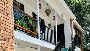 A two-story building with a balcony, a staircase with green and teal steps, and potted plants around the entrance.