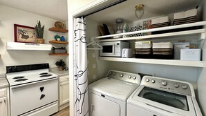 A laundry room with a white stove, a washing machine, and a dryer. There are shelves above with various items.