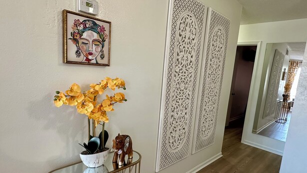 A hallway with a decorative panel, a framed artwork, and a vase with yellow flowers.