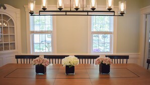 Una mesa de comedor con tres jarrones de flores, una araña y una ventana con persianas.