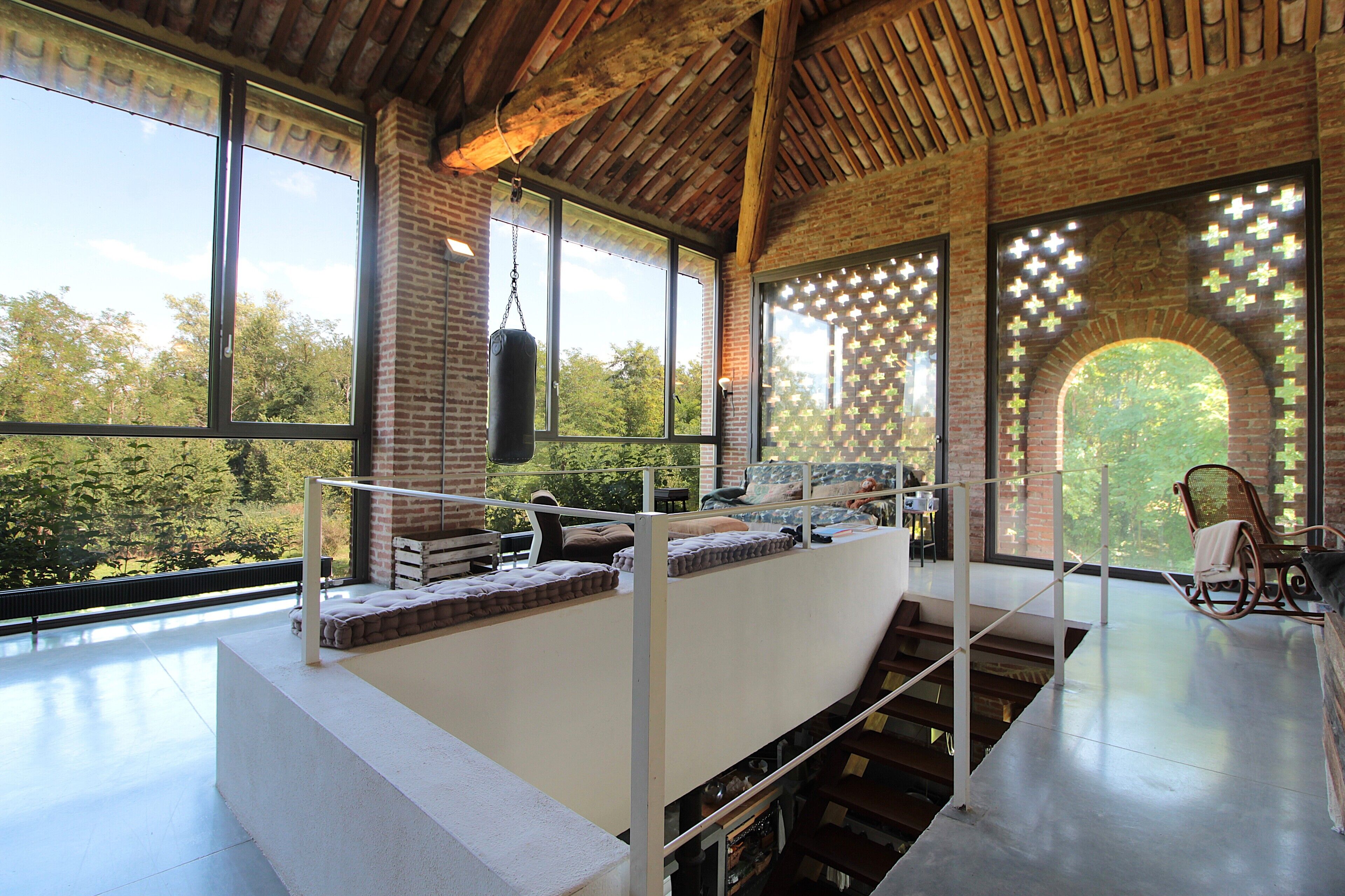 A modern interior with a high ceiling, large windows, a suspended punching bag, and a cozy seating area with cushions.