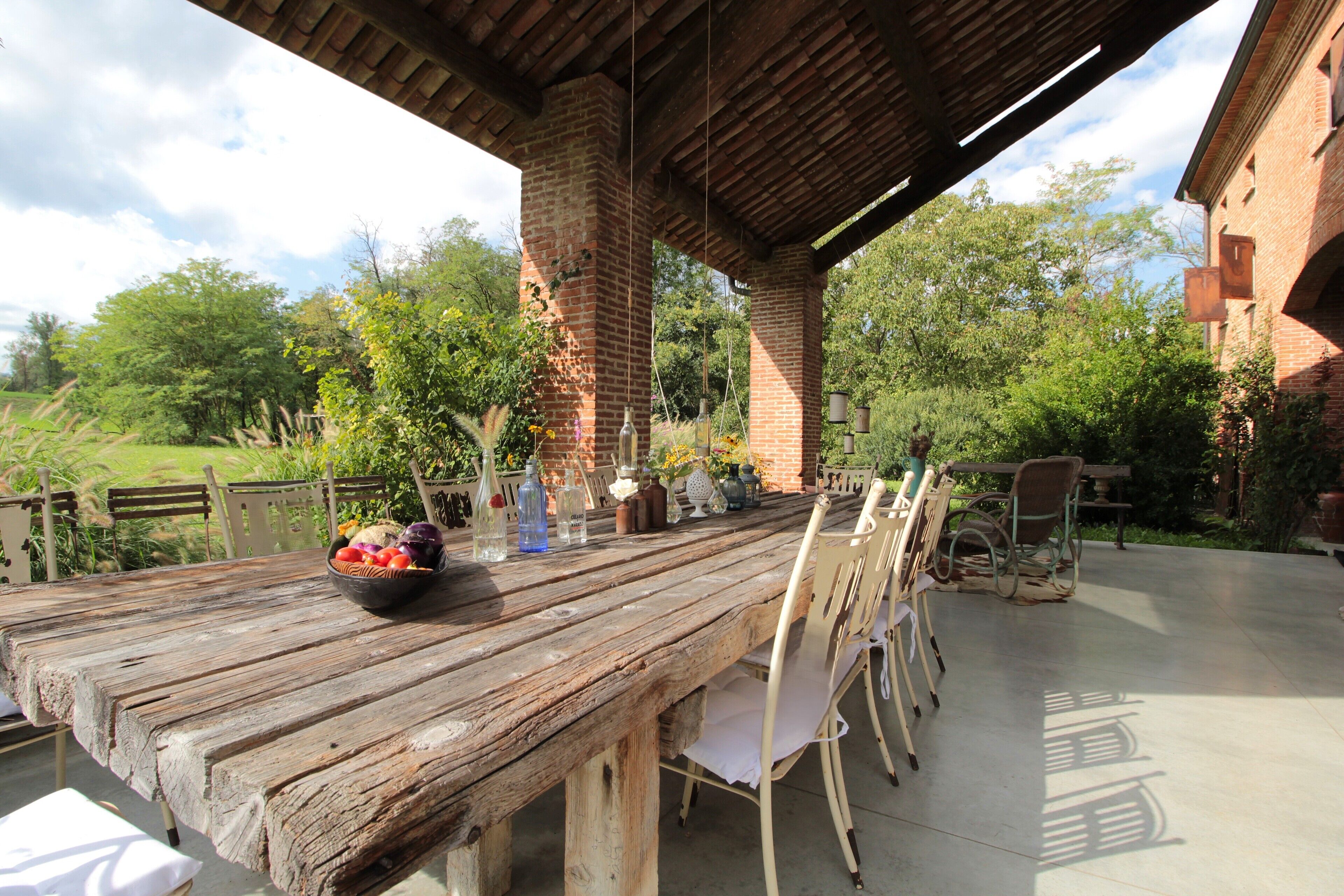 An outdoor wooden table with chairs, a bowl of fruit, and hanging planters.