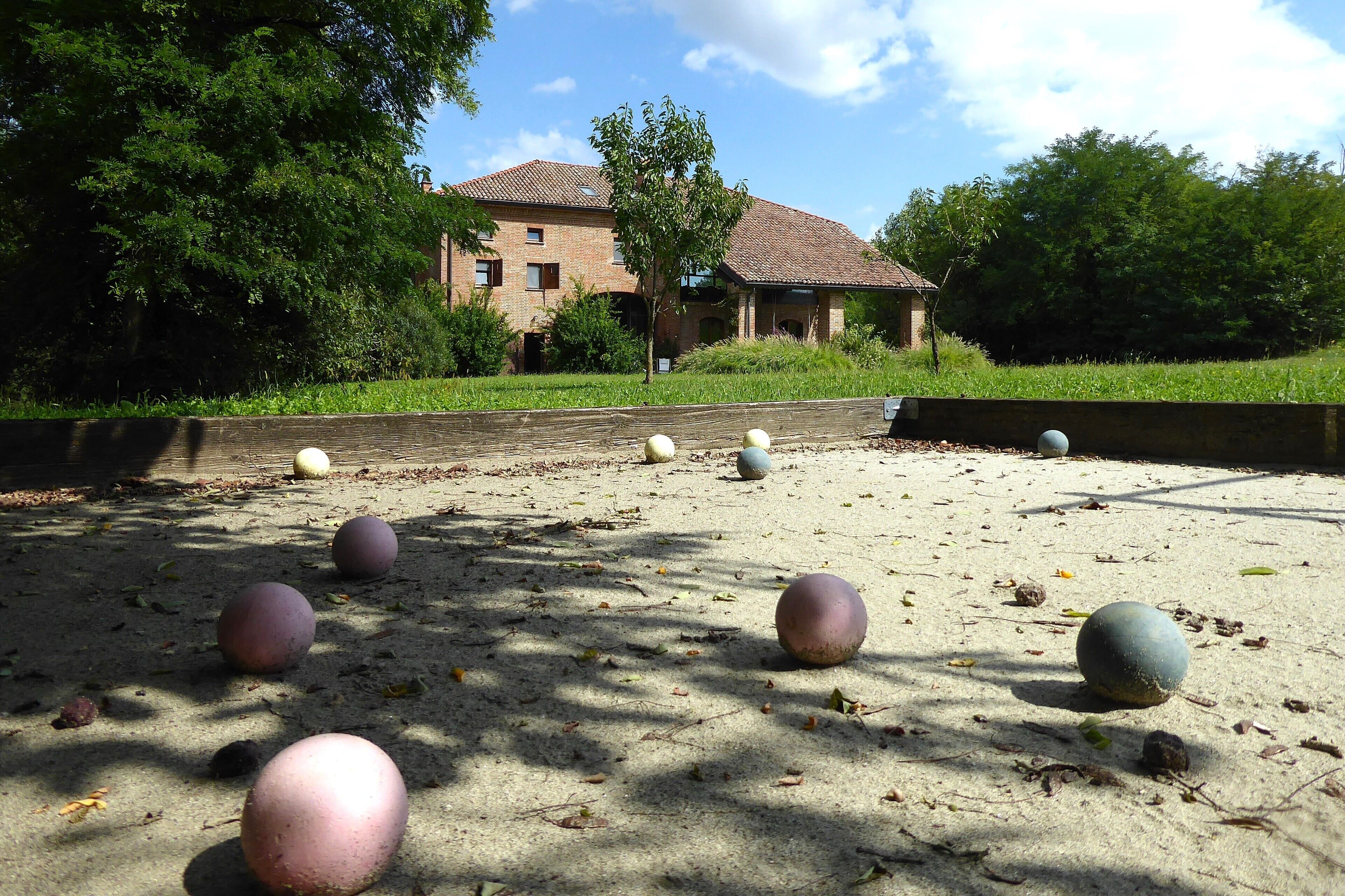 A sandy area with several spherical objects scattered around, surrounded by greenery and a building in the background.