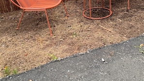 Two orange metal chairs and a small table set on a gravel surface, with a wooden fence in the background. - Apartment in the countryside 30mn from the 24h of Le Mans (Saint-Georges-du-Rosay)