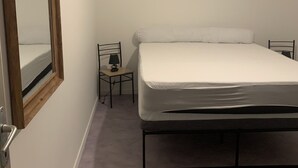 A bedroom with a bed, a small table with a lamp, a chair, and a large mirror on the wall. - Apartment in the countryside 30mn from the 24h of Le Mans (Saint-Georges-du-Rosay)