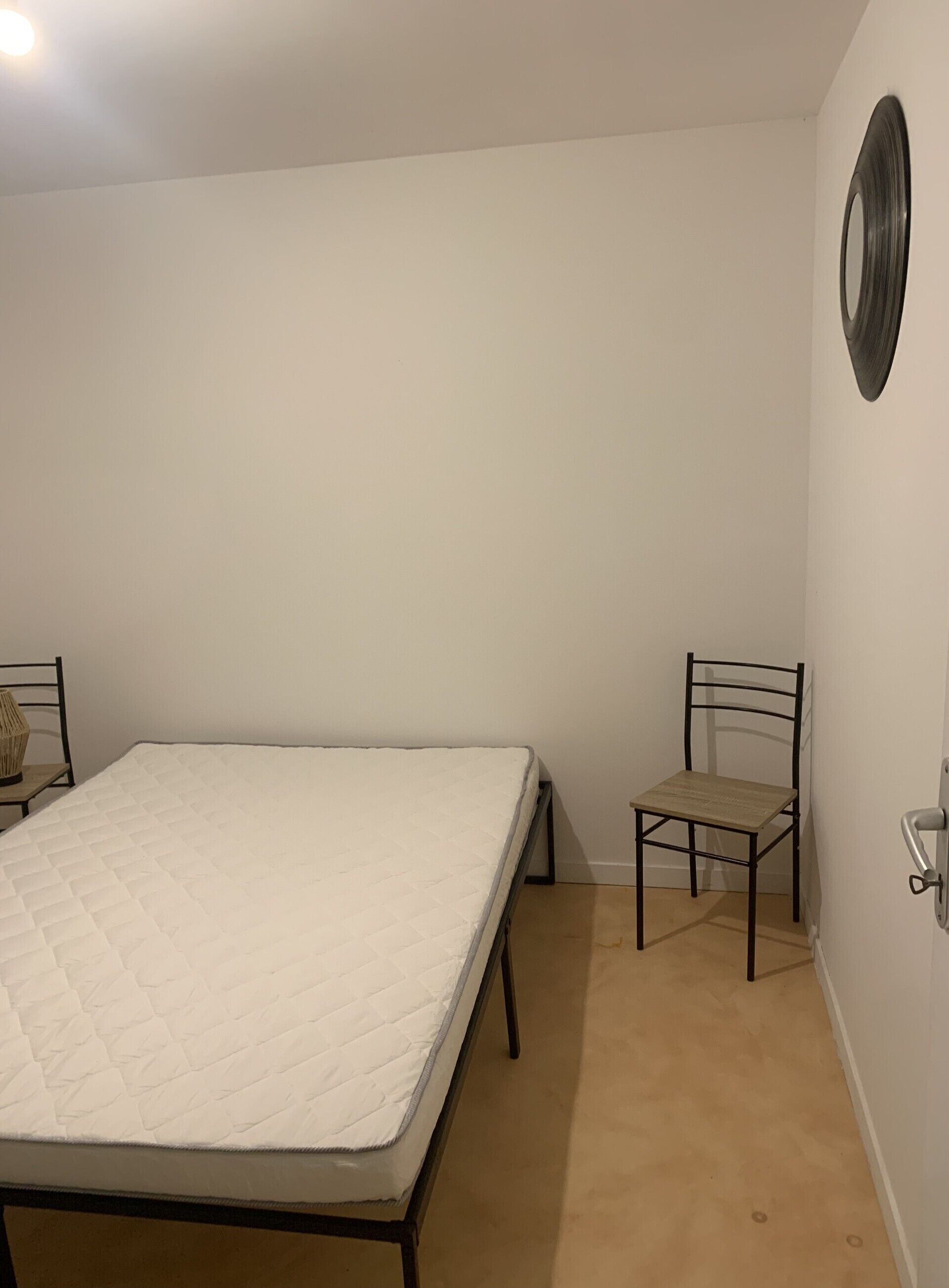 A bedroom with a single bed, a chair, and a wall-mounted mirror.