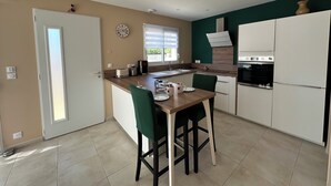 A modern kitchen with a central island, white cabinets, and a green chair. - Bright, quiet house in Redessan (Redessan)