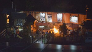Ein Essbereich im Freien mit Feuerstelle, Holzkonstruktionen und umzäunter Gelände.