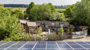 Ein rustikales Holzhaus mit einem umzäunten Garten, Solaranlagen und Blick auf die Landschaft.