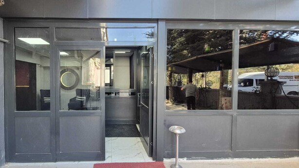 Entrada de um edifício moderno com portas de vidro, espaço interior visível com assentos e uma pessoa do lado de fora.