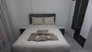 A neatly made bed with a towel arrangement, a grey headboard, and a wardrobe with a black door. - Keyf Suit Rezidans (Nevşehir)
