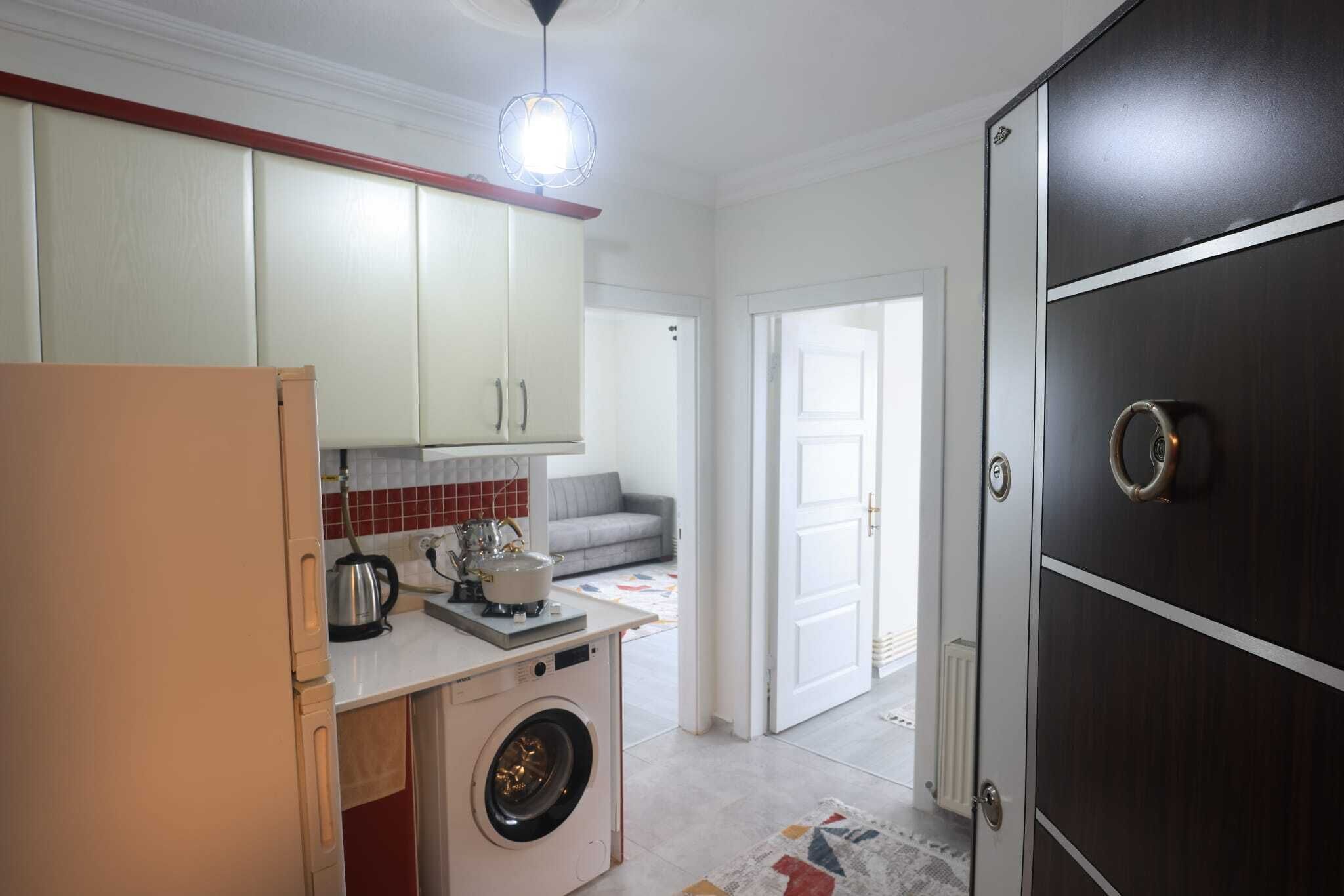 A compact kitchen with a washing machine, a kettle, and a countertop.