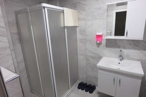 A bathroom with a glass-enclosed shower, a white sink with a mirror above it, and a pair of shoes on the floor. - Keyf Suit Rezidans (Nevşehir)