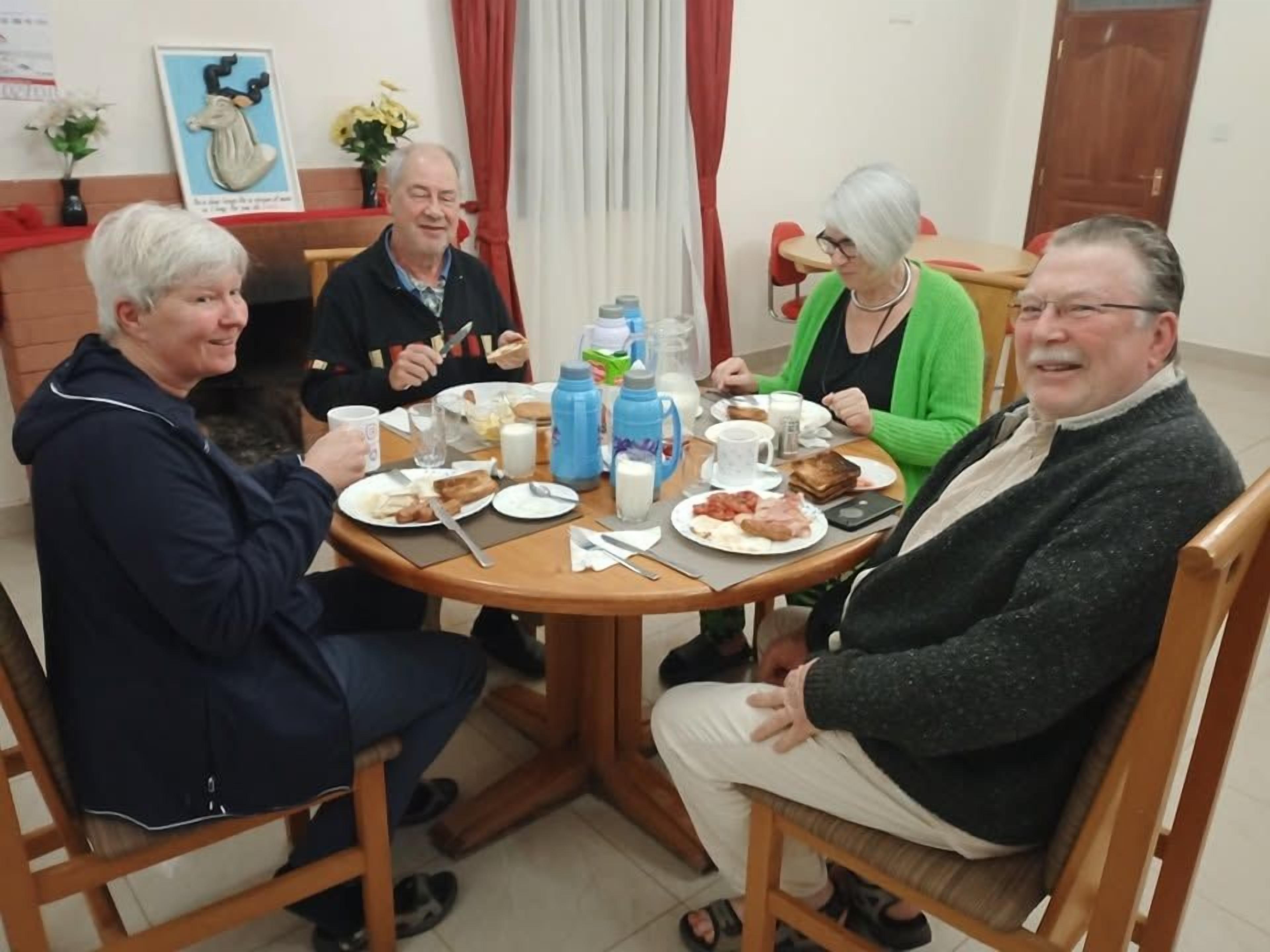 A group of people seated around a round table with plates of food, cups, and a water bottle.