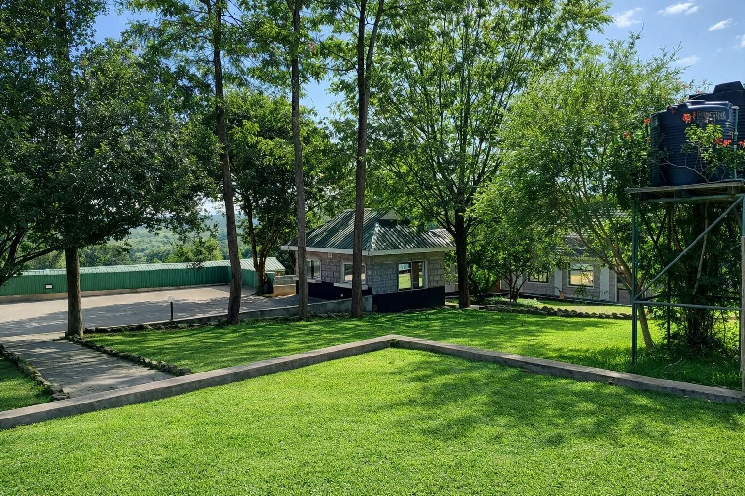 Zona verde con un edificio, árboles y una cerca verde.