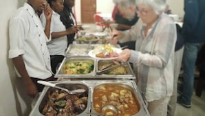 A buffet with various dishes and a group of people serving themselves.