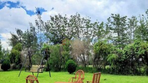 A grassy outdoor area with a swing set and four wicker chairs.