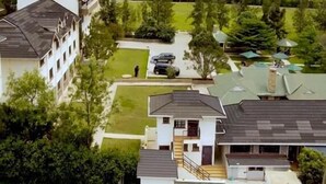A residential area with multiple houses, a central pathway, and a hilly landscape in the background.