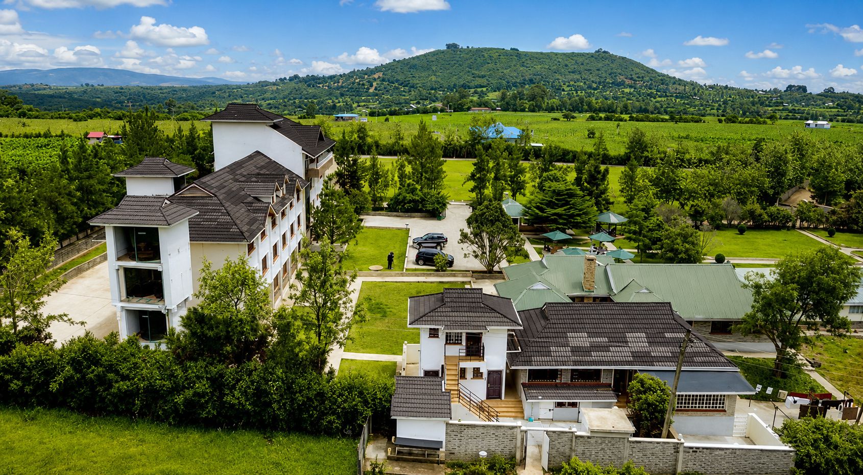 A residential area with multi-story buildings, a green lawn, and a hilly landscape in the background.