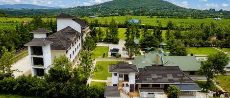 A residential area with multi-story buildings, a green lawn, and a hilly landscape in the background.