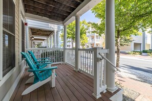 A porch with a wooden floor, white railings, and two turquoise Adirondack chairs.