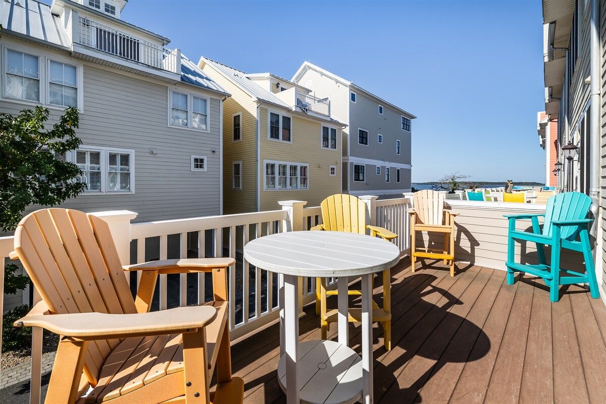 A deck with outdoor seating, including chairs and a table, overlooking a residential area with multi-story buildings.