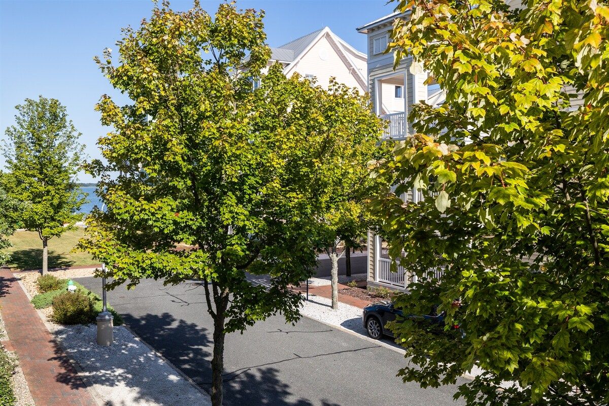 Une rue résidentielle bordée de maisons et d’arbres, avec un ciel dégagé.