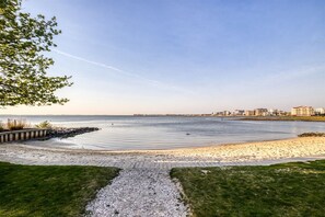 A coastal walkway leading to a beach with a clear view of the ocean and distant buildings. - Sunset Island 43 Sunset Island Drive (Ocean City)