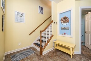 A staircase with wooden railings and a yellow bench in a hallway with a tiled floor.