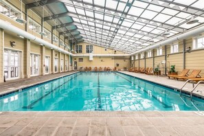 An indoor swimming pool with a high ceiling and skylights, surrounded by lounge chairs and a tiled floor. - Sunset Island 43 Sunset Island Drive (Ocean City)