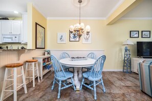 A dining area with a white table and blue chairs, a chandelier, and a kitchen in the background. - Sunset Island 43 Sunset Island Drive (Ocean City)