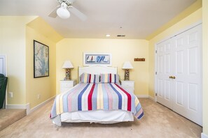 A bedroom with a bed, two bedside tables, a ceiling fan, a door, and a wall-mounted artwork. - Sunset Island 43 Sunset Island Drive (Ocean City)