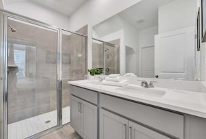 Un baño moderno con cabina de ducha de vidrio, un espejo grande y un mueble de tocador doble.