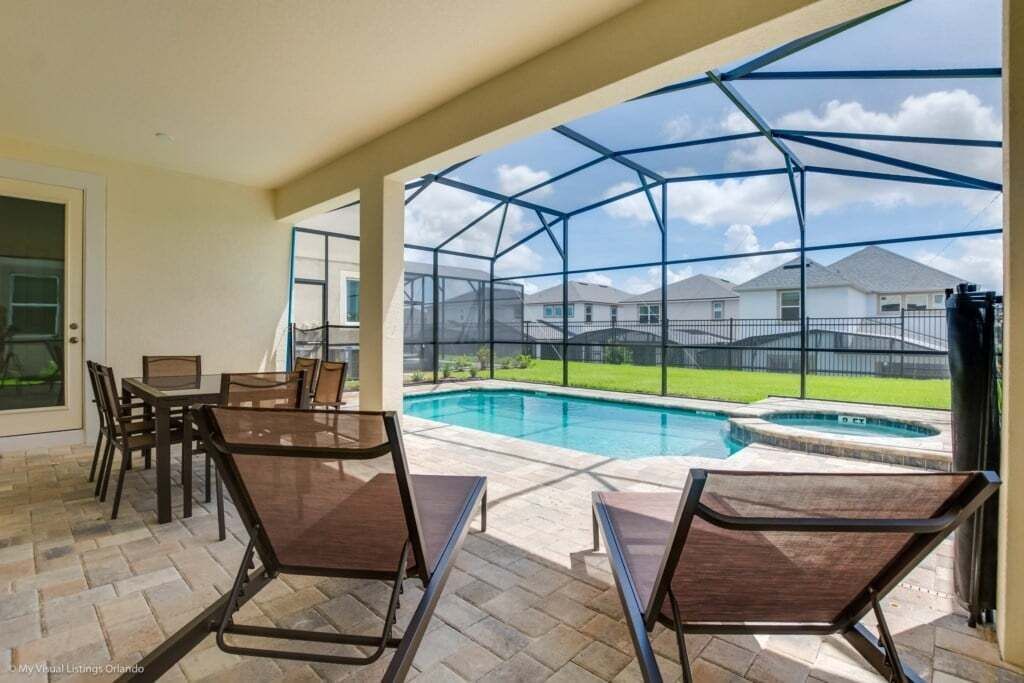 A covered patio with a pool, outdoor seating, and a view of neighboring houses.
