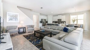A spacious living room with a large sectional sofa, a coffee table, and a TV. There is a staircase leading to the upper floor. - Orlando Newest Resort Villa With Pool 1791spp 4 Bedroom Home (Kissimmee)