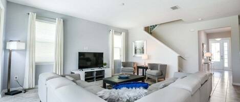Una sala de estar moderna con un amplio sofá modular en forma de L, un televisor de pantalla plana y una escalera que sube a otro nivel.