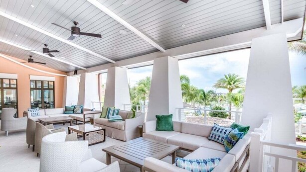 A covered outdoor seating area with sofas, chairs, and tables, featuring ceiling fans and large windows overlooking a landscaped area. - 1513nassau 5 Bedroom Villa (Kissimmee)