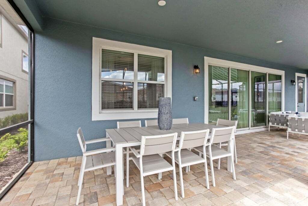 Une terrasse extérieure avec une table et des chaises, une grande fenêtre et une porte à panneaux de verre.