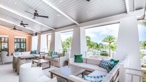 A covered outdoor seating area with sofas, chairs, and tables, featuring ceiling fans and large windows overlooking a landscaped area. - Solara 1787 Cvt 6br Villa W/ Pool & Luxury Spa 6 Bedroom Villa (Kissimmee)