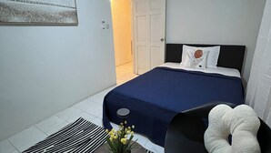 A bedroom with a bed, a chair, a small table with a vase, and a zebra-patterned rug.