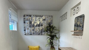 A small, well-lit room with a tiled floor, a wooden bench with a yellow cushion, a potted plant, and a wooden shelf unit.