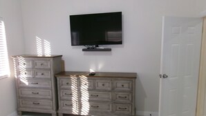A bedroom with a white dresser, a television mounted on the wall, and a closed door.