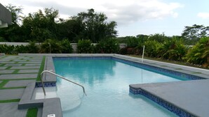 A rectangular pool with a blue tiled edge, surrounded by a concrete deck with green artificial grass.