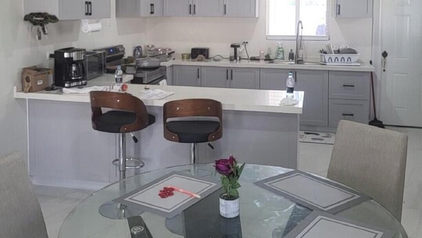 A modern kitchen with grey cabinets, a central island with stools, and a glass dining table.